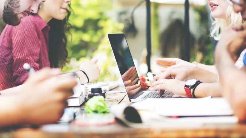 Junge Menschen sitzen gemeinsam am Tisch und arbeiten