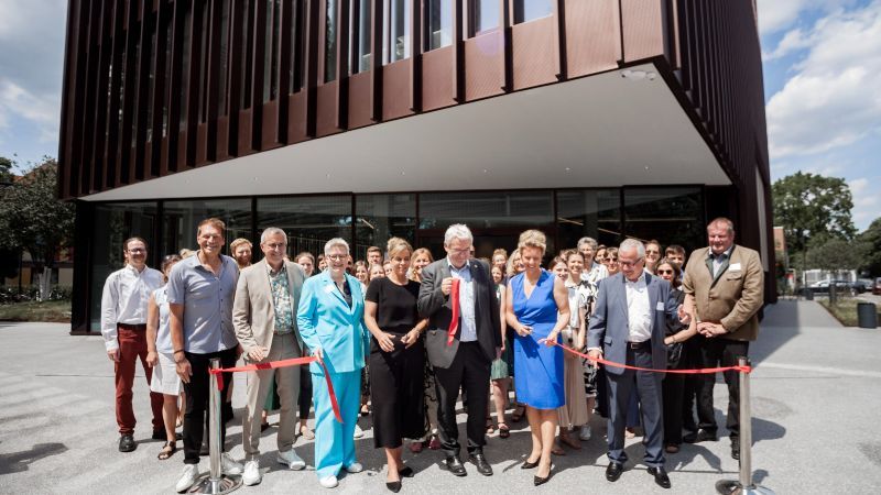 Eine Gruppe von Menschen durchschneidet ein rotes Band vor einem Gebäude