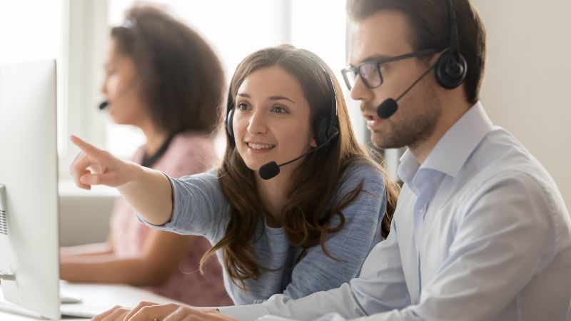 Frau mit Headset hilft Mann und zeigt auf den Bildschirm