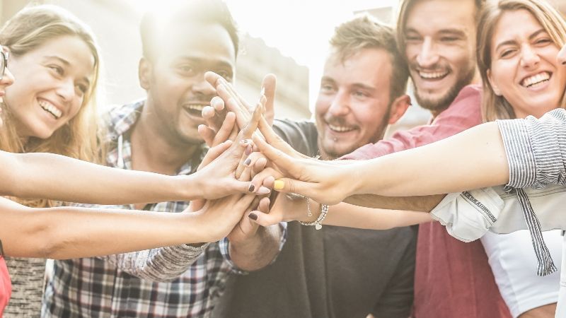 Junge glückliche Menschen führen in ihrer Mitte Hände zusammen